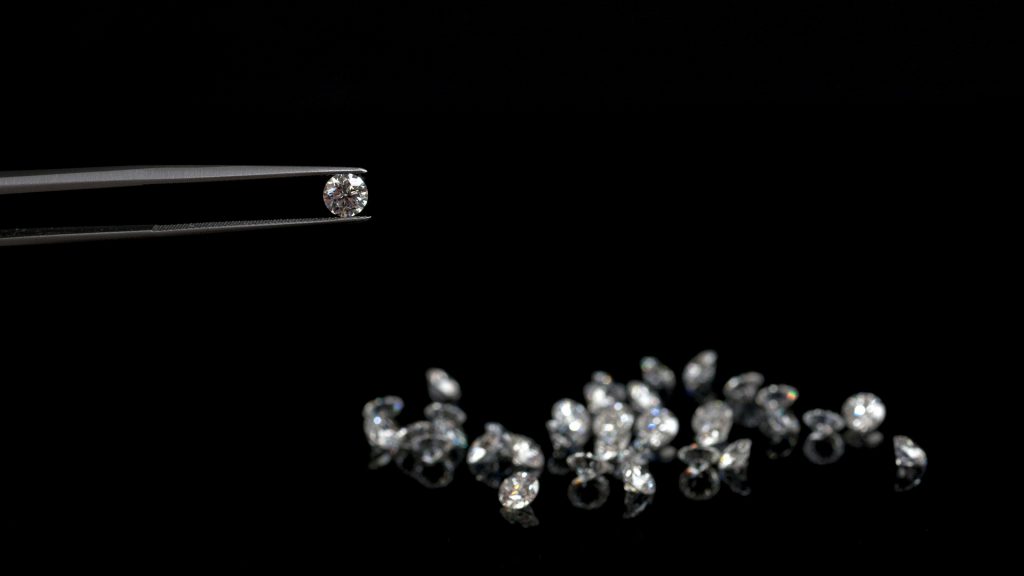 Tweezers Holding Ideal Cut Melee Diamond with More Diamonds in the Background